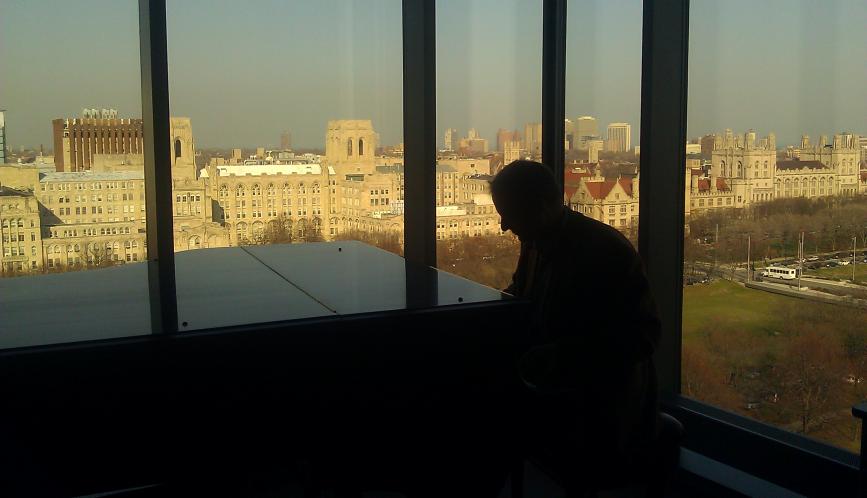 Someone in silhouette standing at the window, with the University of Chicago campus seen through the windows.