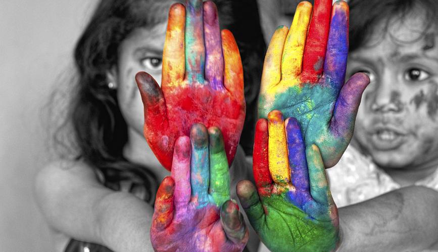 A stock image of two children in black and white, with their hands outstretched and covered in multicolored paint.