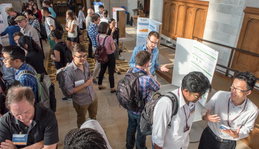 An overhead image of a room of students and faculty in conversation during poster sessions.