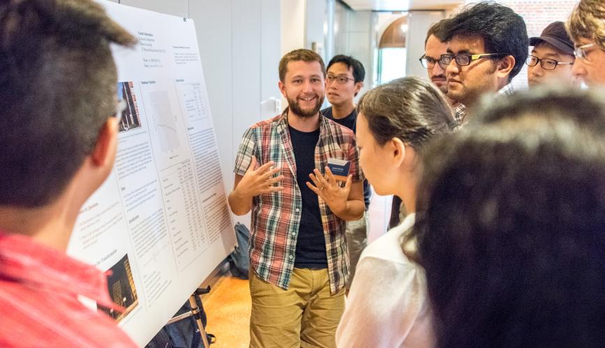 A group of students listen as another student presents his poster.