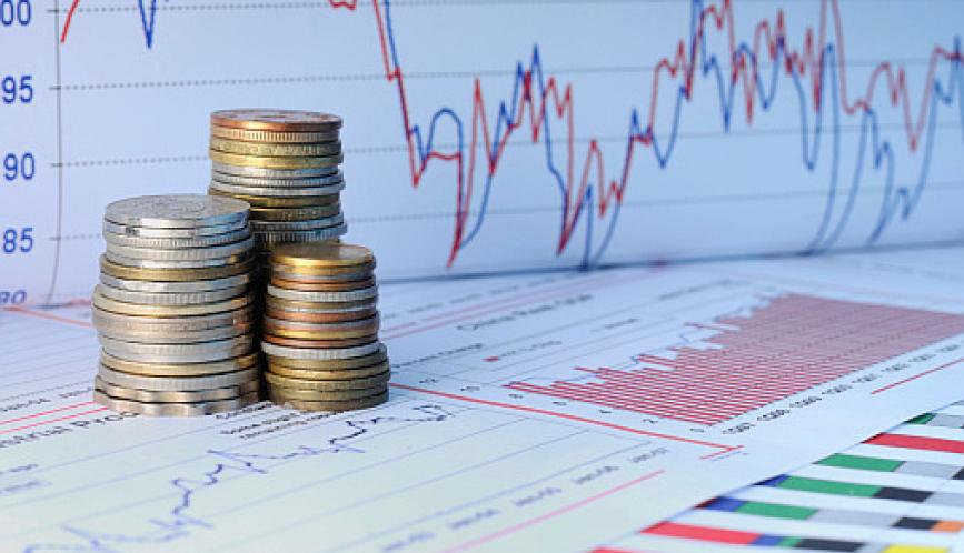 A stock image of three stacks of coins sitting amid colorful graphs and charts.
