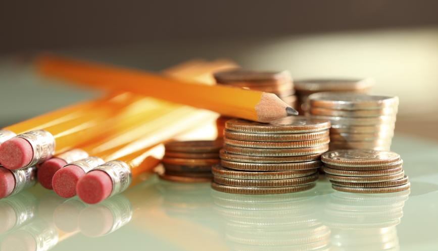 A stock image of pencils sitting beside small stacks of quarters and other change.
