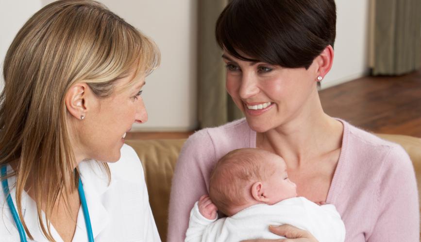 A stock image of a mother holding a baby, seated beside a doctor wearing a stethoscope.