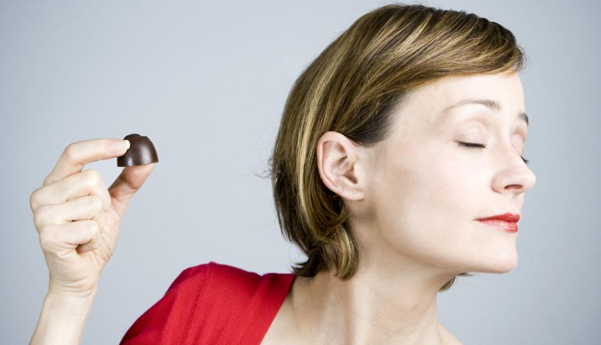 A stock image of a woman holding up a chocolate, but her face is turned away from it.