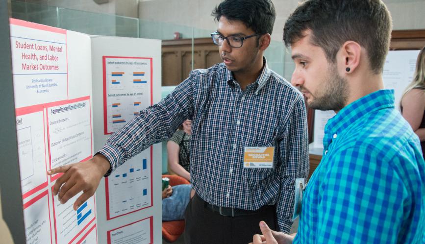 A student presents hris work during poster sessions, while another student listen.