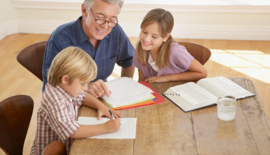 A grandfather helping two grandchildren study at the kitchen table.