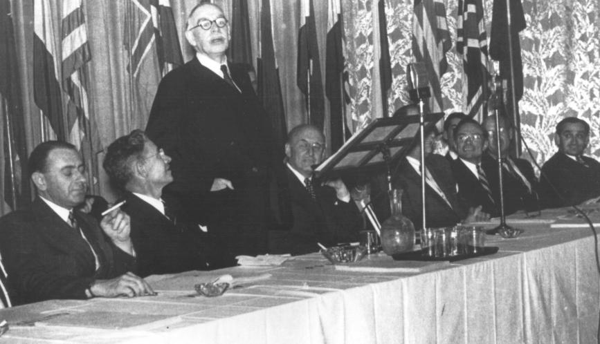 A black and white photo showing John Maynard Keynes standing at a formal event table