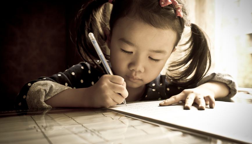 Young girl writing with pen and paper.