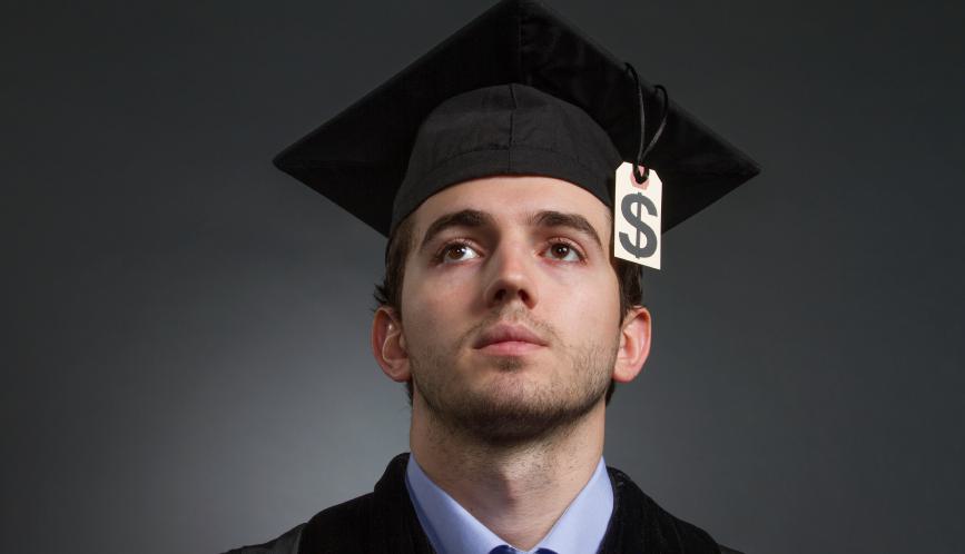 Man wearing graduation attire with a dollar sign hanging from his cap.