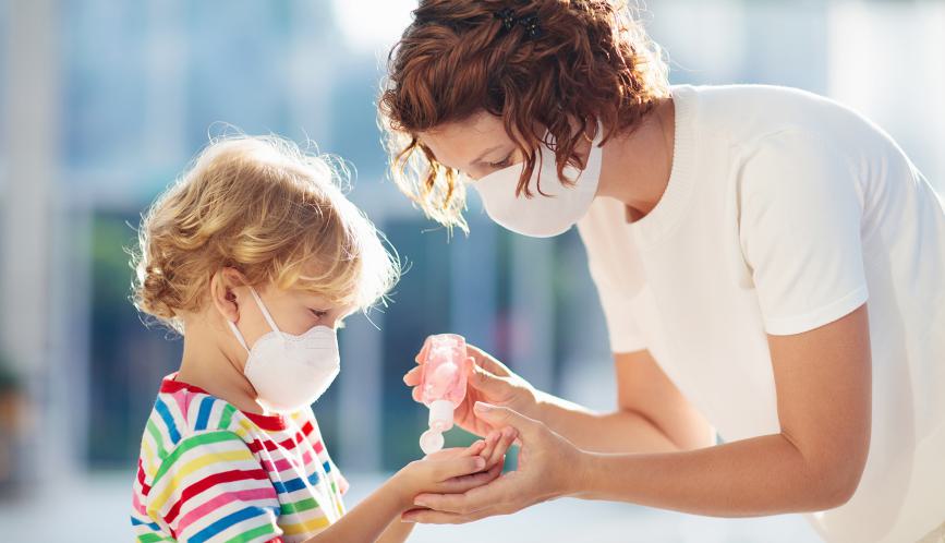 Adult giving a young child hand sanitizer, both are wearing masks.