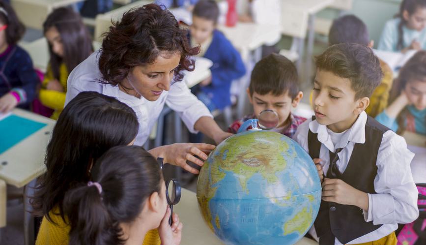 School children and teacher looking at a globe in a classroom.