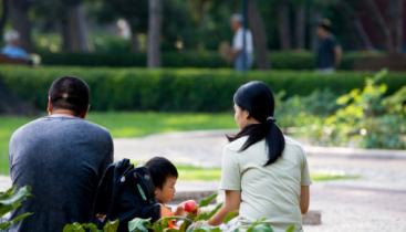 A man, woman, and child sitting outside in a park, seen from behind.