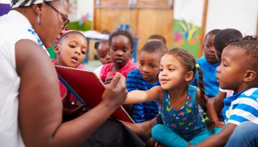Stock image of a teacher reading a book to a group of preschool students.