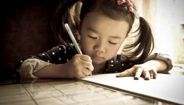 Young girl writing with pen and paper.