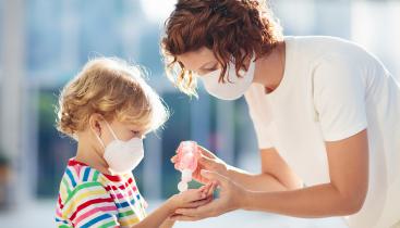 Adult giving a young child hand sanitizer, both are wearing masks.