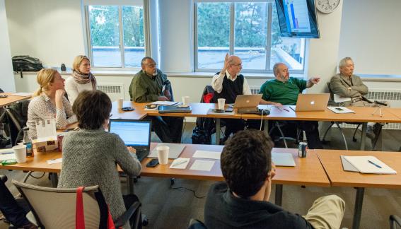 Conference participants at a U-shaped table, listening to a presentation