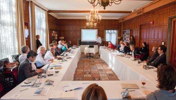 A full room image of the conference, featuring attendees seated at a U-shaped table.