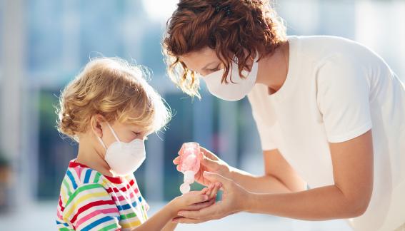 Adult giving a young child hand sanitizer, both are wearing masks.